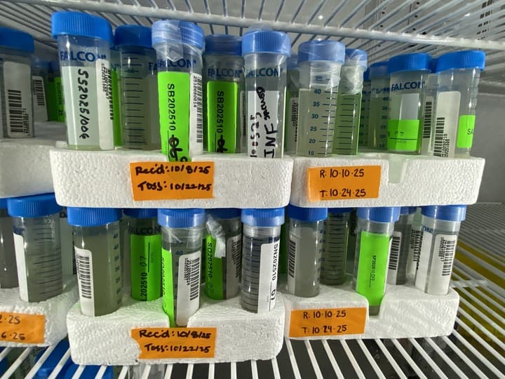 A white shelf with several containers of various sizes and shapes, containing wastewater. The containers are labeled with information, indicating their contents and possibly their purpose or usage. The shelf is organized in a way that allows easy access and visibility of the items.