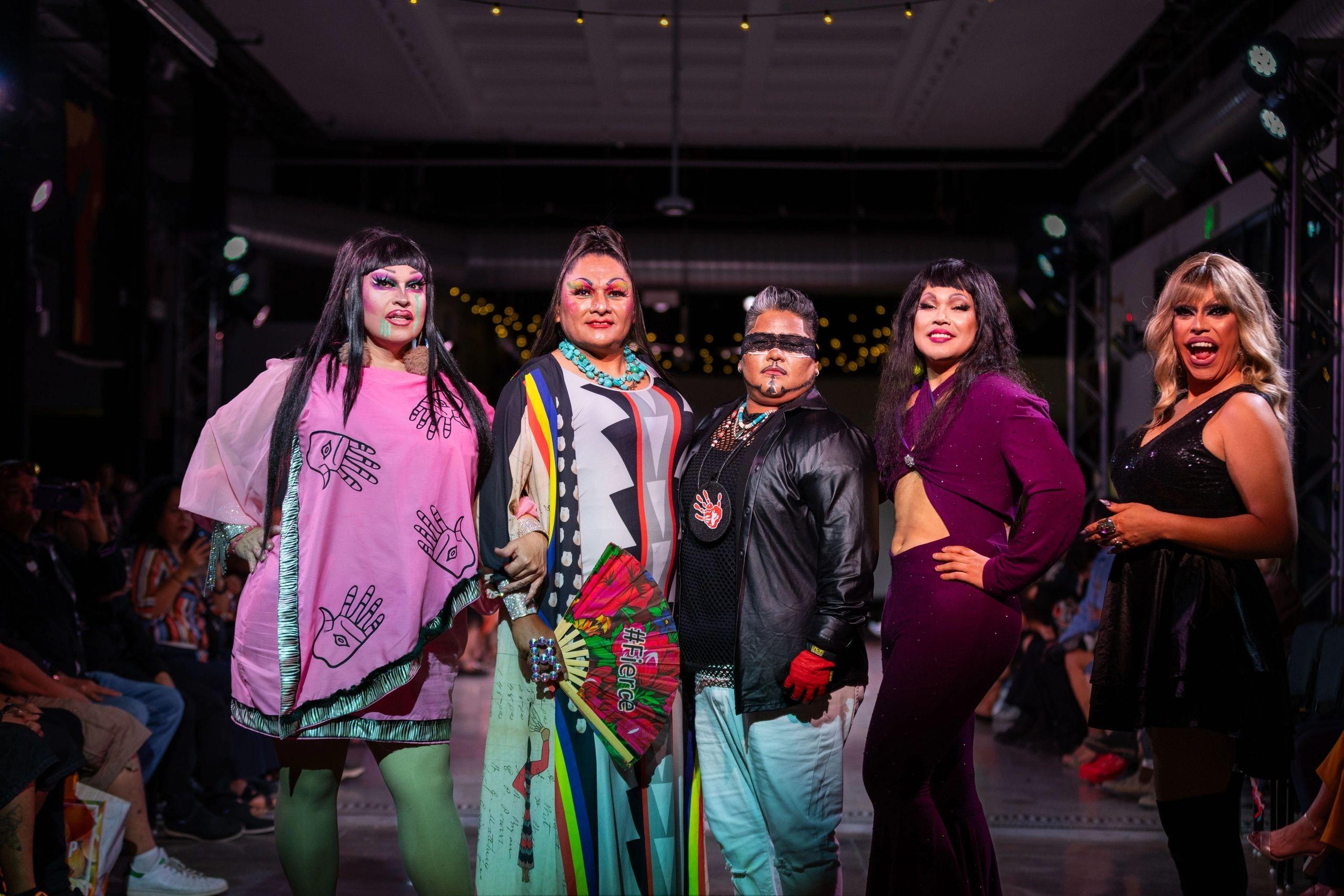five adults standing side by side, dressed up in makeup and fashionable clothes