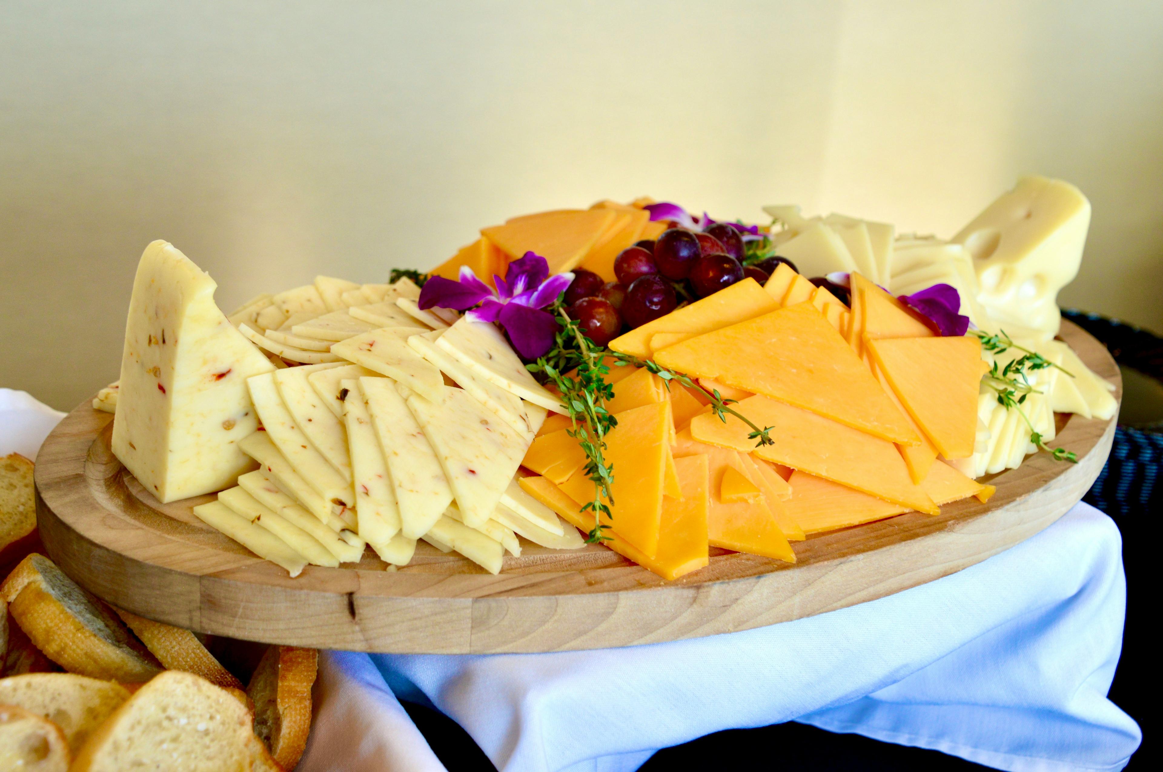 Cheese plate served on a wooden board with a variety of cheeses and some garnishes.