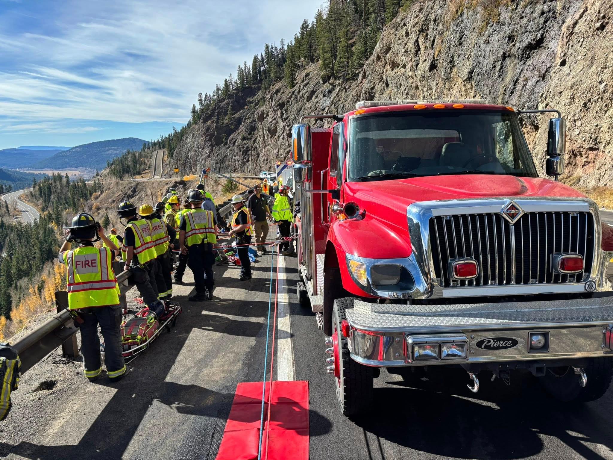 A red fire truck is parked on the side of a road, with a group of people standing around it. The scene appears to be a rescue operation, with the fire truck possibly involved in aiding the people. The people are wearing safety vests.