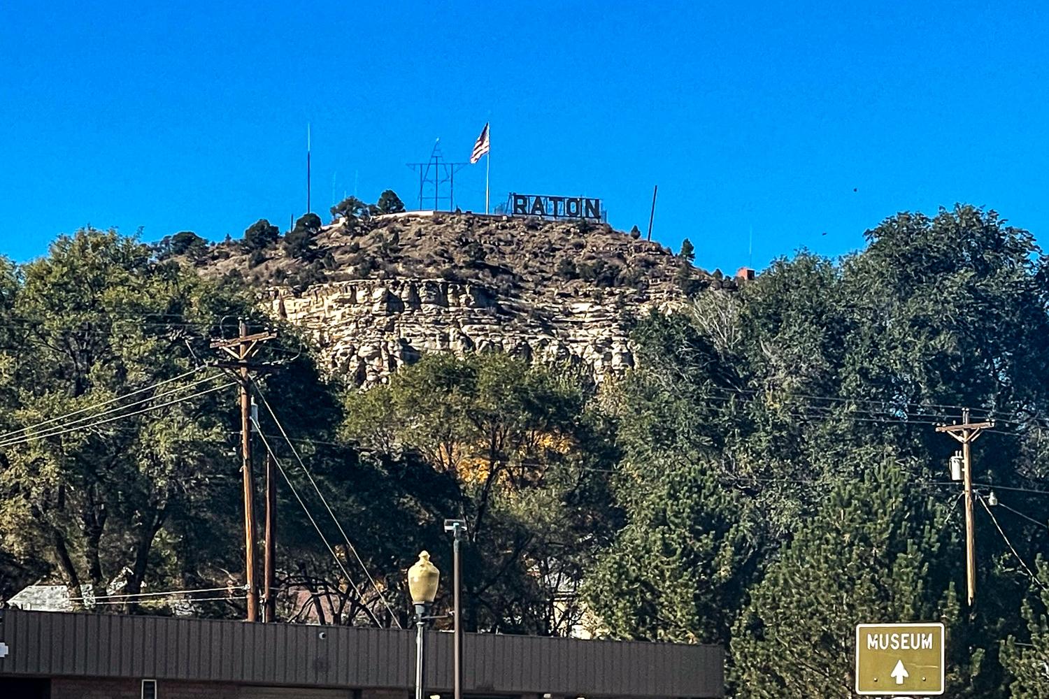 A photo of a small rocky butte with the city sign of Raton on it.