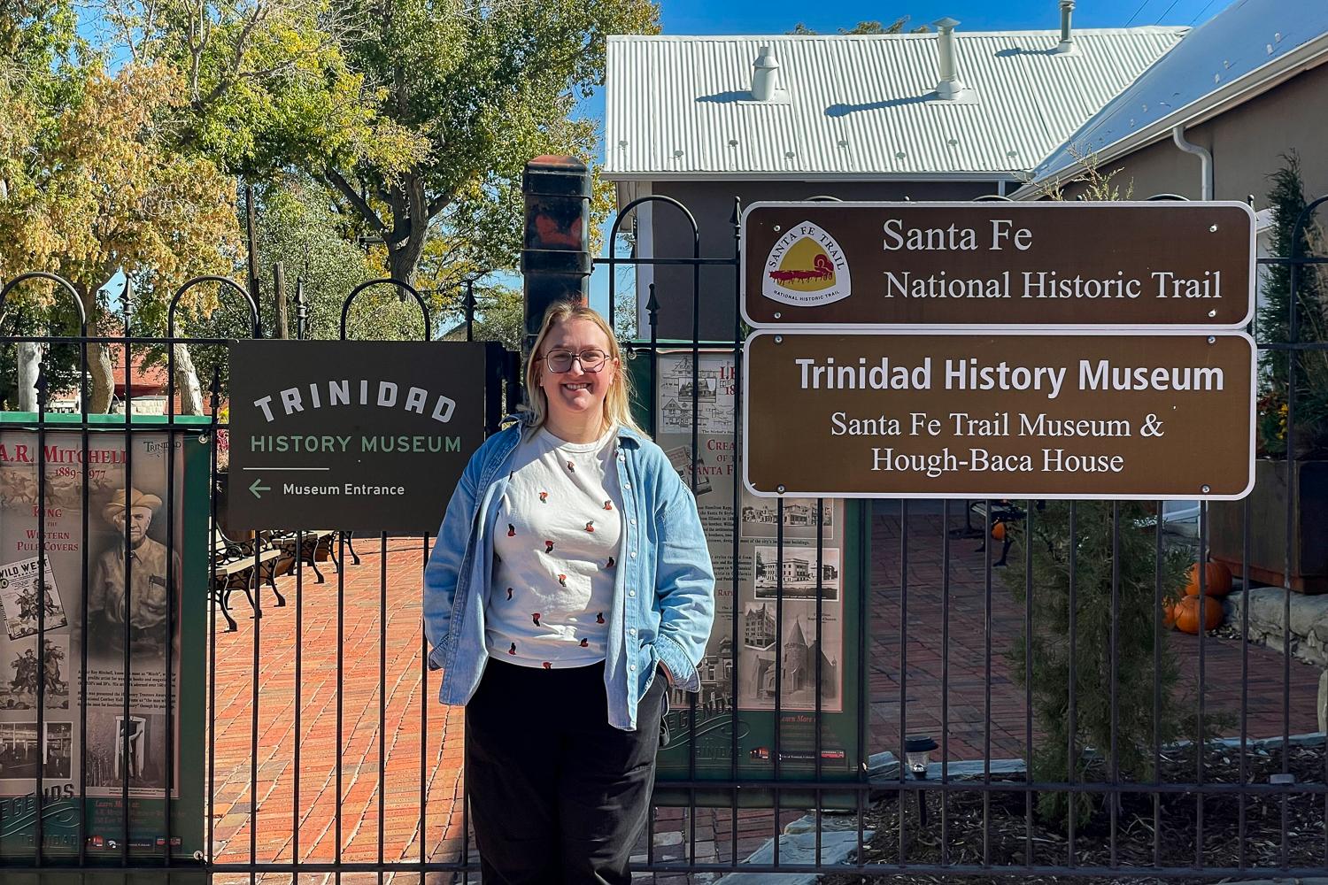 A woman stands outside of the gate of the Trinidad History Museum. She has blond hair.