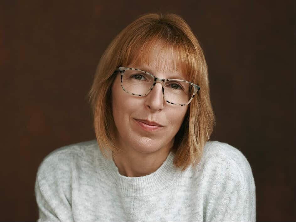 Photo is ahead and shoulders image of a woman with shoulder length hair and glasses.