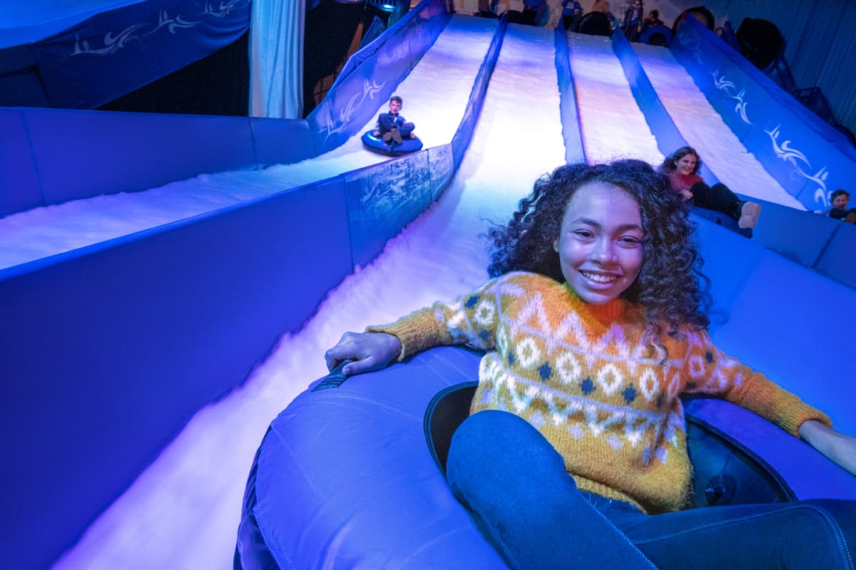 Kids zoom down an indoor tuning hill, smiling and having fun.