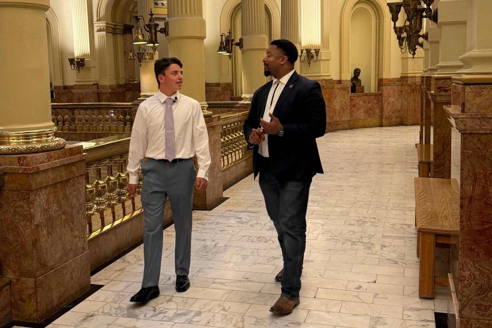 Image shows a teenager on the left and a man on the right in a walkway at the state capitol.