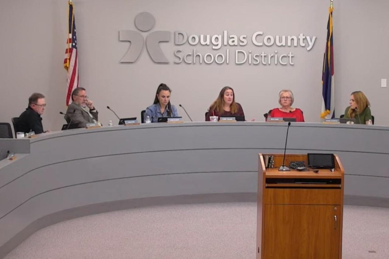 A screen picture of seven member of the Douglas County School District board, each sitting behind a microphone on a curved desk.