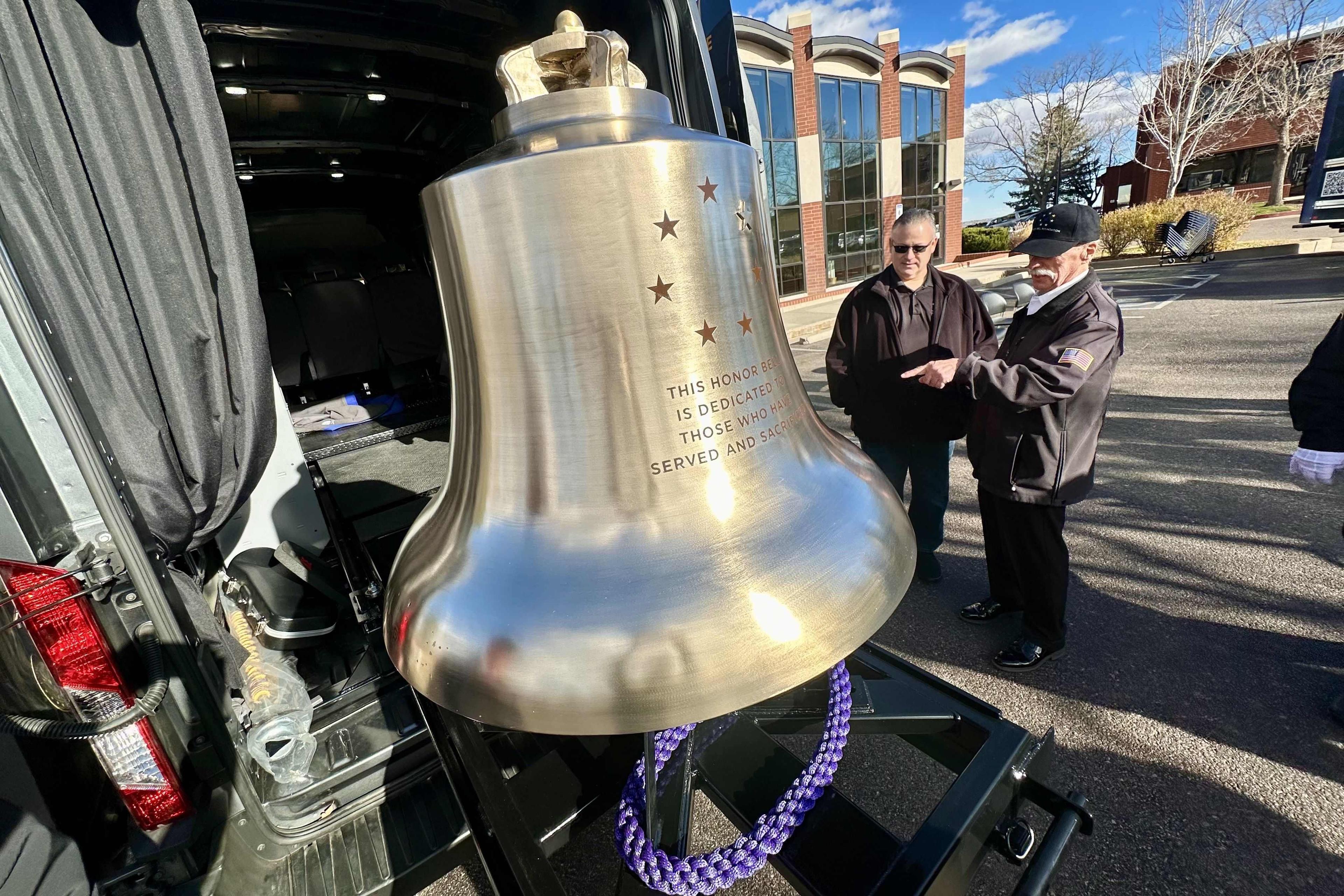A large bronze bell is mounted onto a sliding shelf attached to a van outside.