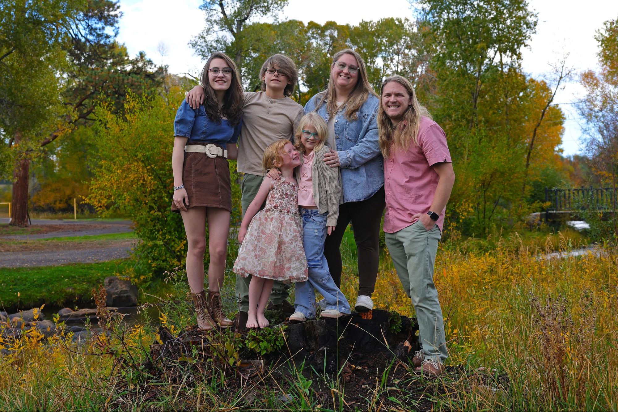 family of six -- two parents, four kids -- posing with foliage of leaves and trees in the background.