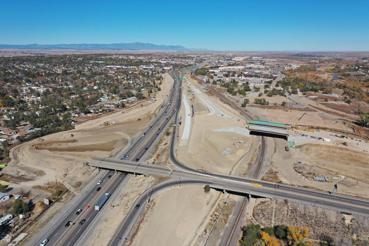 Aerial view of four lane highway with traffic and interchange construction area, surrounded by a suburban city landscape.