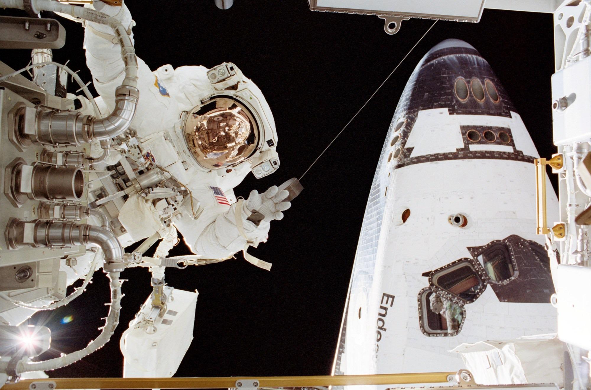 Astronaut John Herrington, in a full space suit, waves to the camera as he floats outside a space craft.