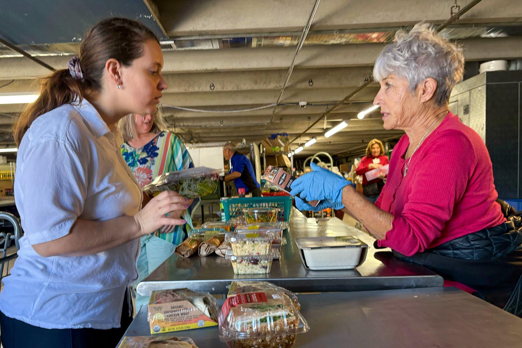 Two people speak over a counter with food on the counter