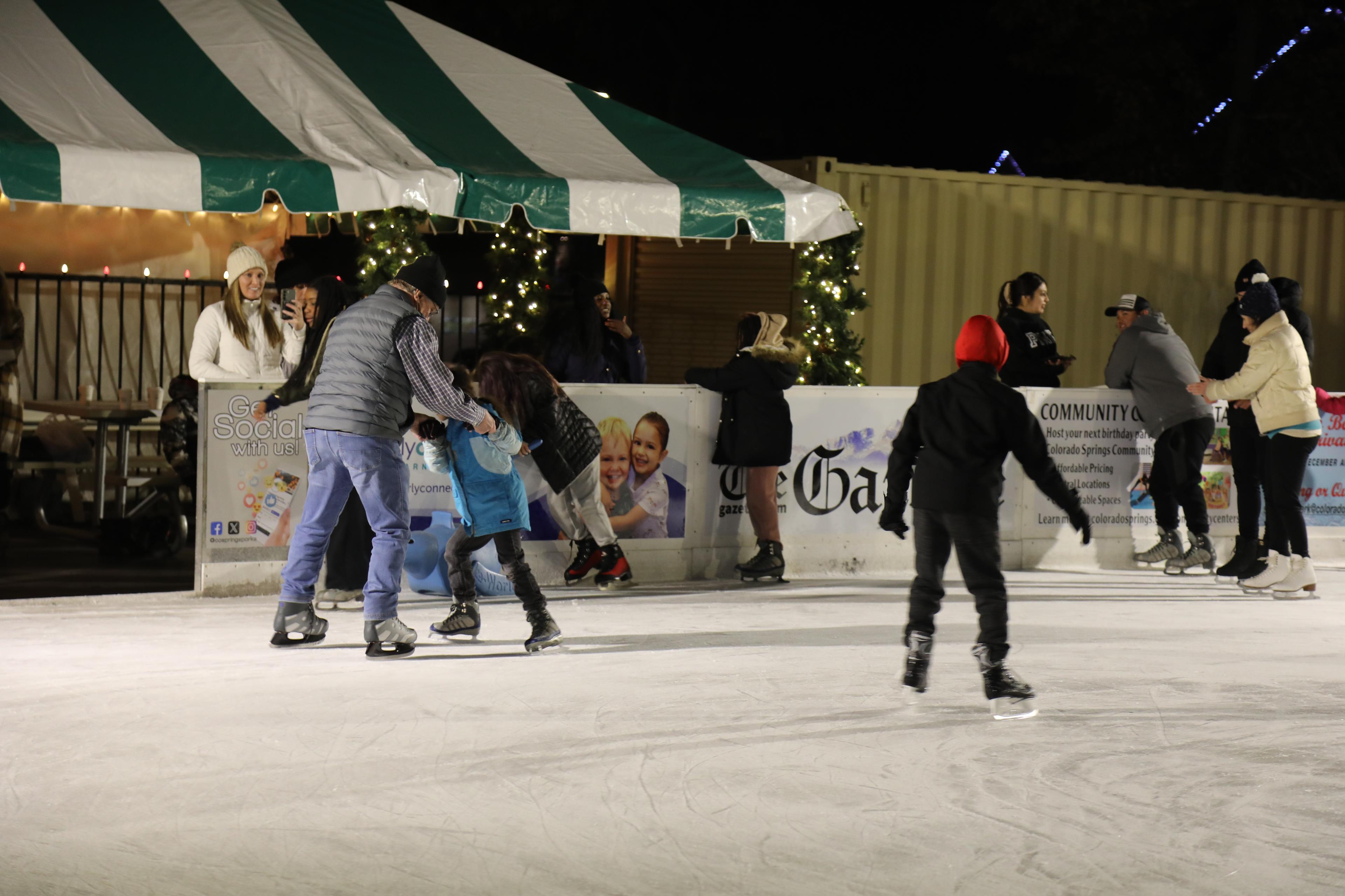 A group of children and adults ice skate at an outdoor skating rink.