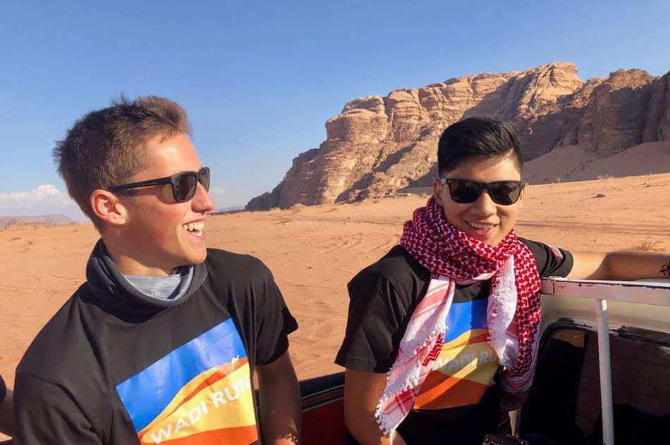 Two men are sitting in a vehicle, wearing sunglasses and black shirts. They are smiling and enjoying their time together.