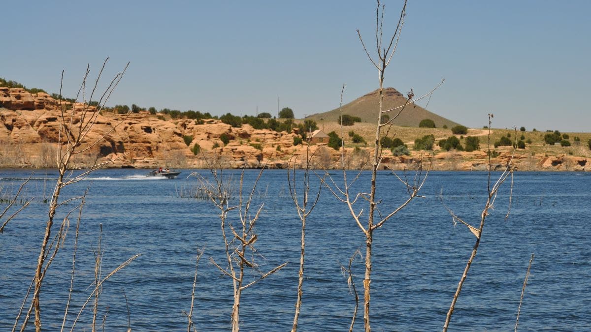 A boat speeds across a Colorado reservoir with ocre cliffs and a lone hill in the background.