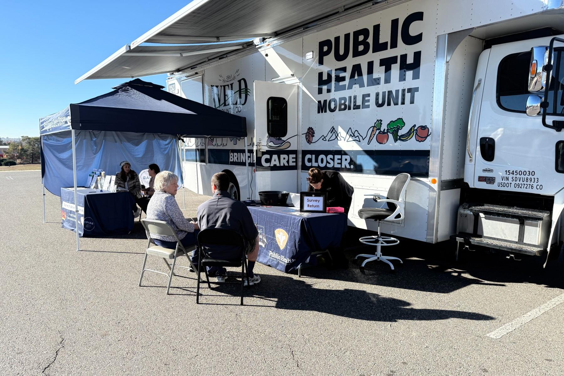 A worker looks at a table while two people seated across from her talk.