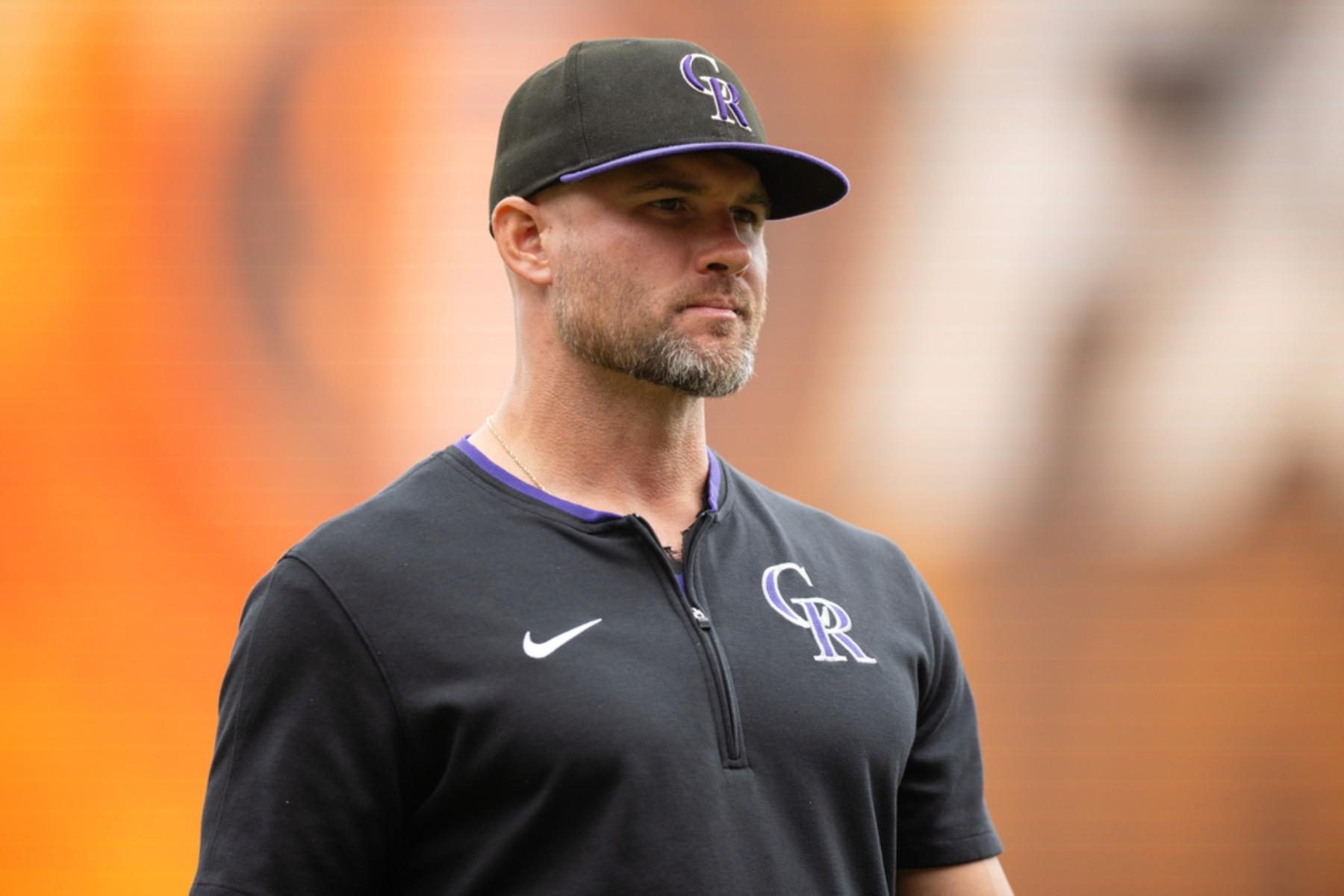 A man wearing a black Nike shirt and a purple and white cap stands in a field, looking off to the side.