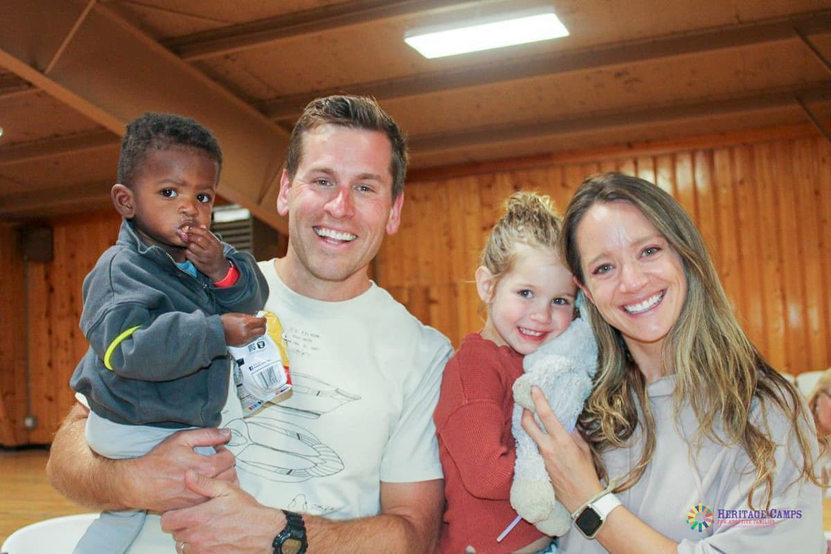 Photo shows a man holding a toddler boy to the left of a woman holding a young girl. They are all smiling at the camera for a family portrait.