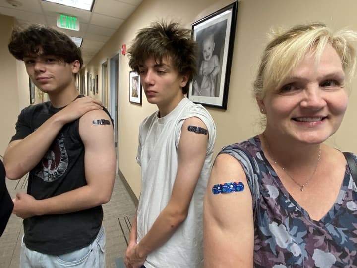 Three people are standing in a room, each with a bandage on their arm. They are posing for a picture.