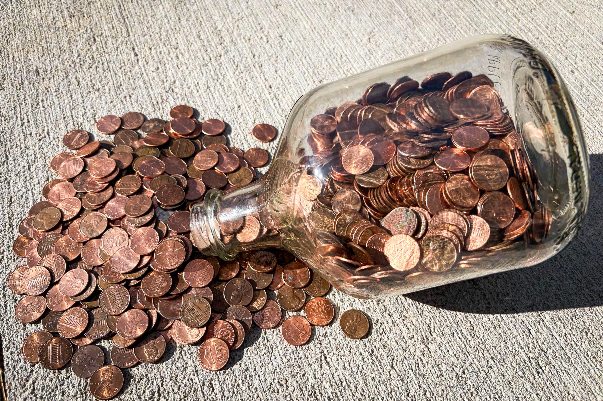 Pennies spilled on a table from a glass bottle