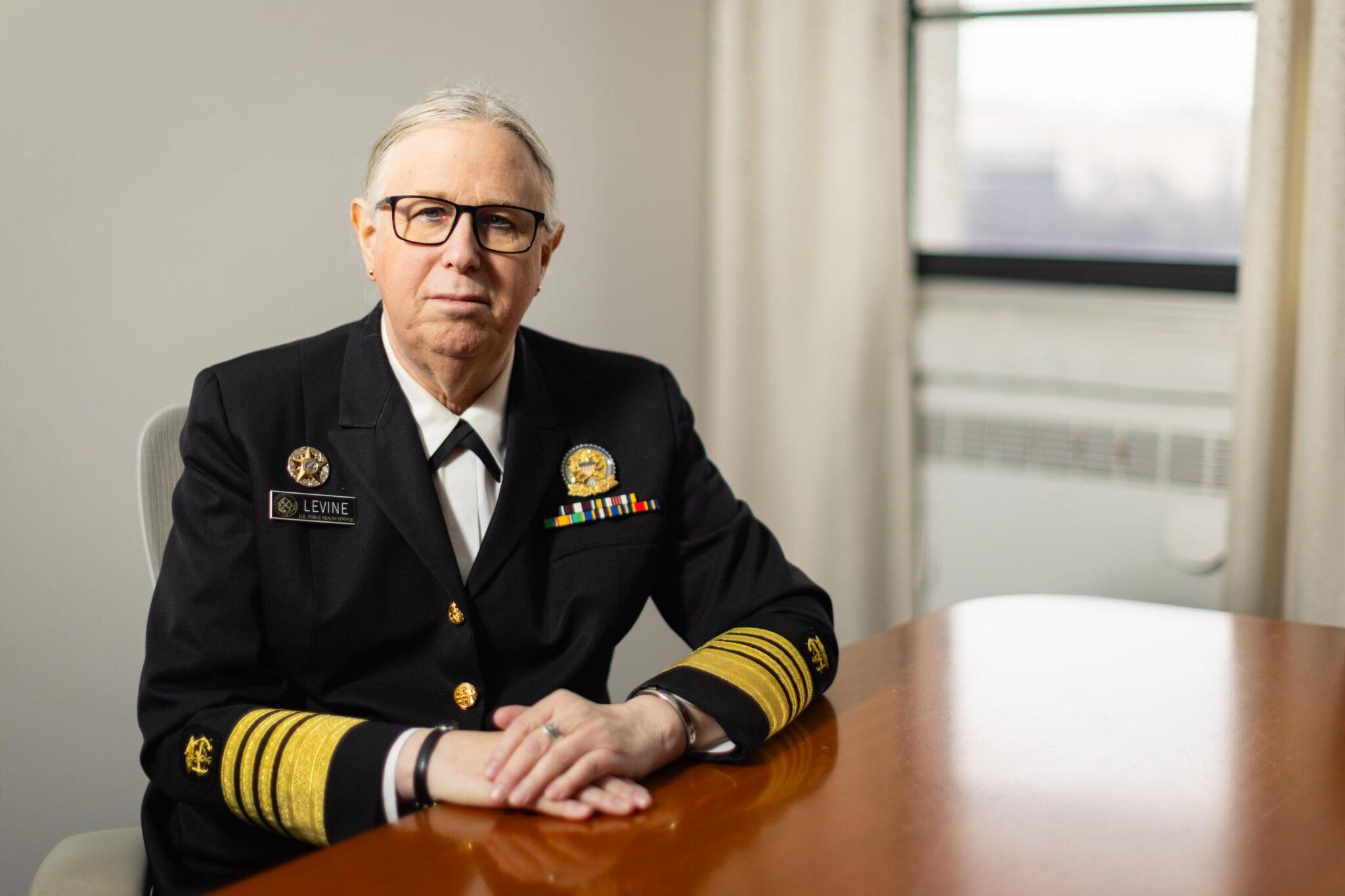 Admiral Rachel L. Levine is a trans woman in her mid 60s. She has glasses and gray hair pulled back from her face. She is wearing a uniform with many gold stripes on the sleeves indicating her high rank.