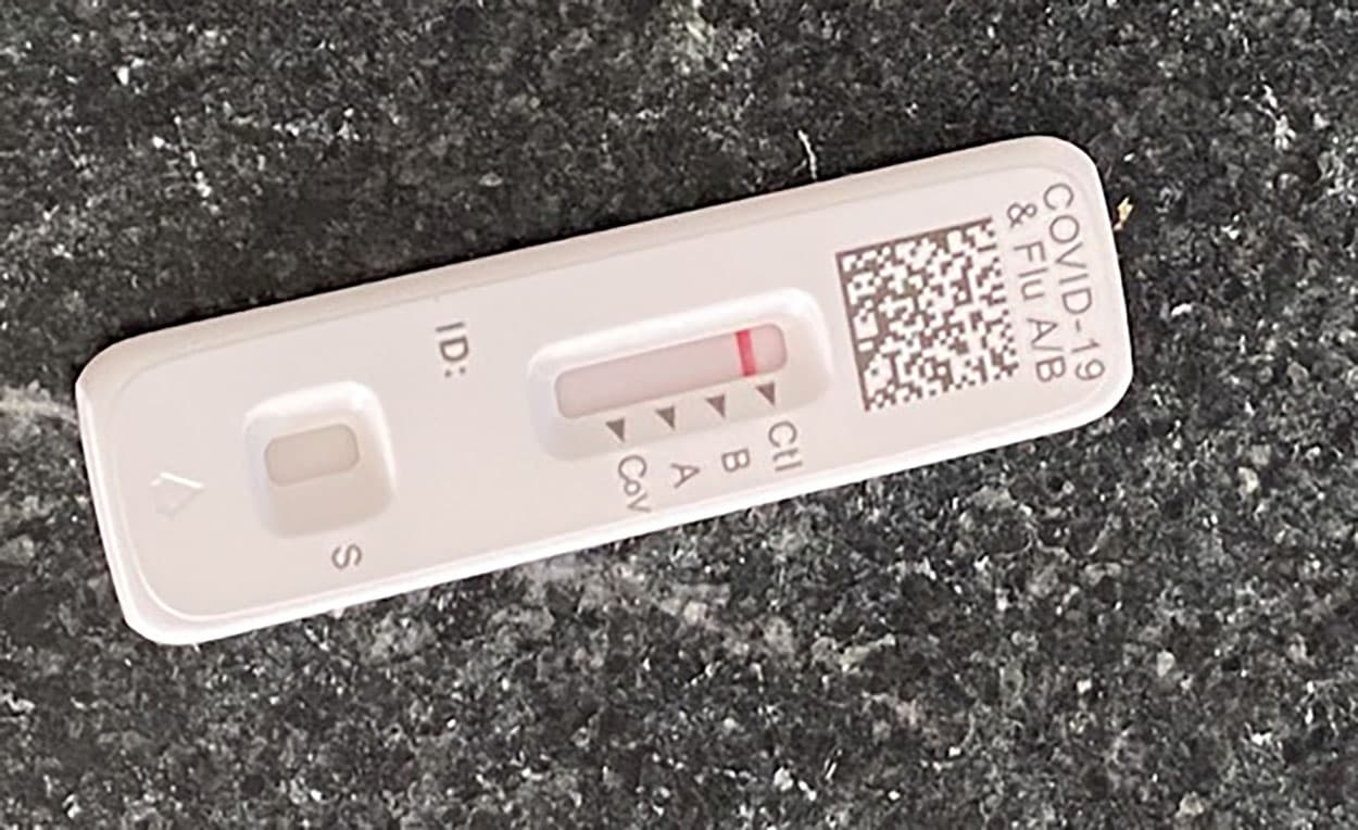 A white medical device with a red dot on it is placed on a black surface. The device is designed to test for influenza type A and B and COVID-19.