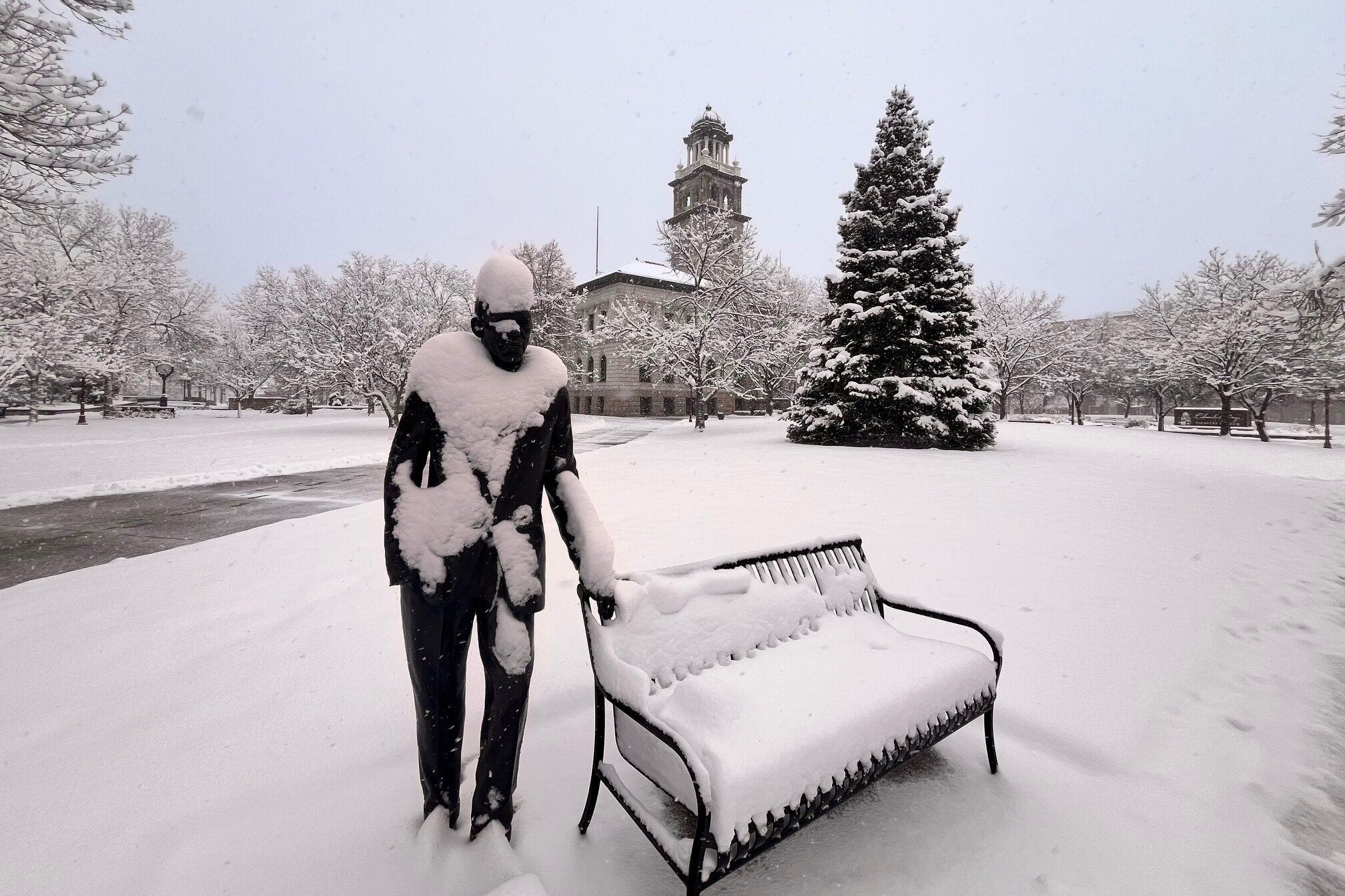 Snow on a bench and statue and blankets green space