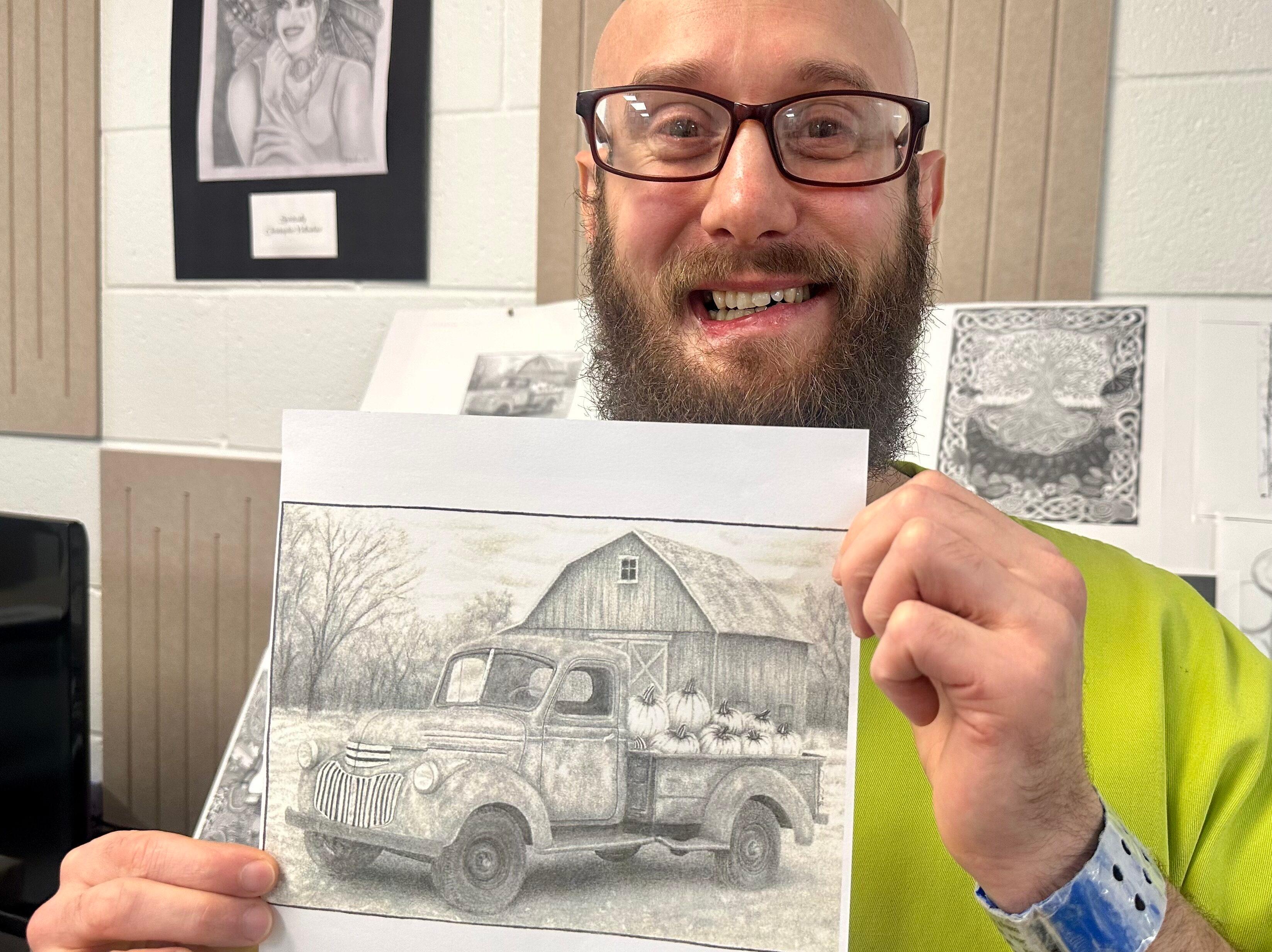 Photo shows a bald man with glasses and a beard smiling in a lime green shirt. He his holding a pencil sketch in front of him of a farm truck filled with pumpkins parked in front of a barn.