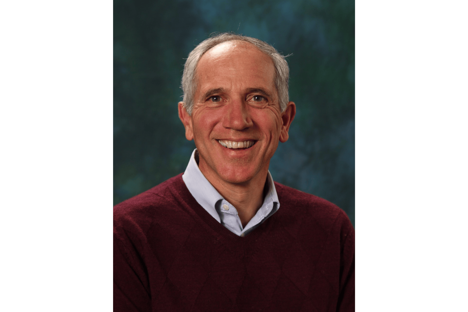 A man with a maroon sweater smiling at the camera