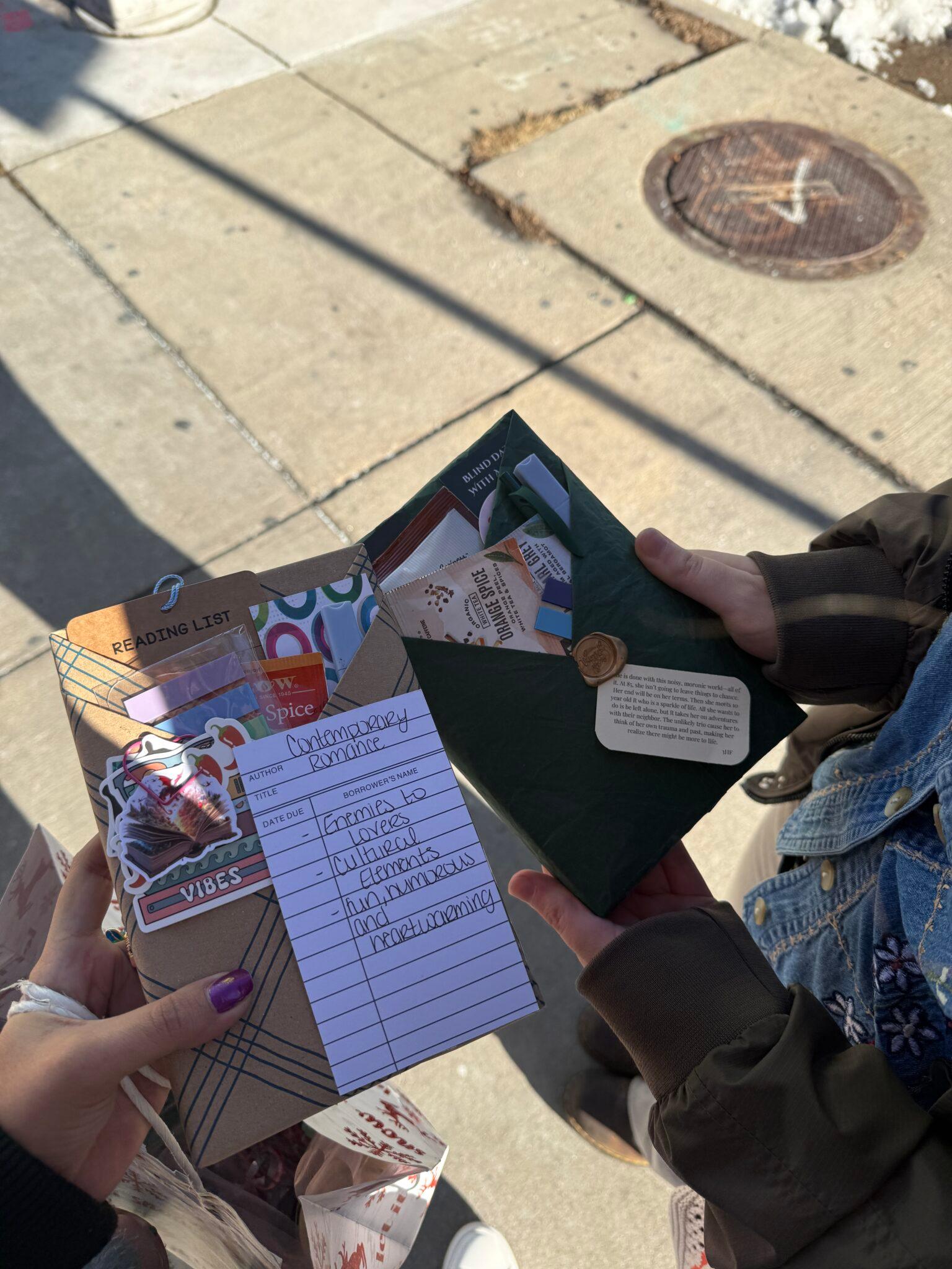 Two people hold books and display their covers. Only their hands and arms are visible.