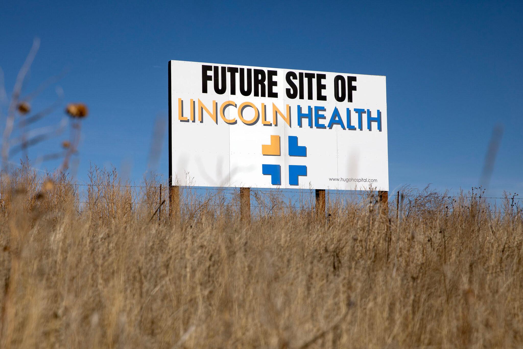 A sign reads "FUTURE SITE OF LINCOLN HEALTH" in big black, yellow and blue lettering. It stands in a field of dead weeds.