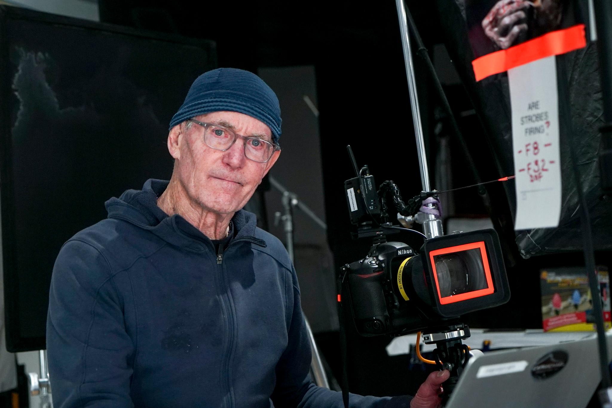 A man wearing glasses and a skull cap holds a camera rig.