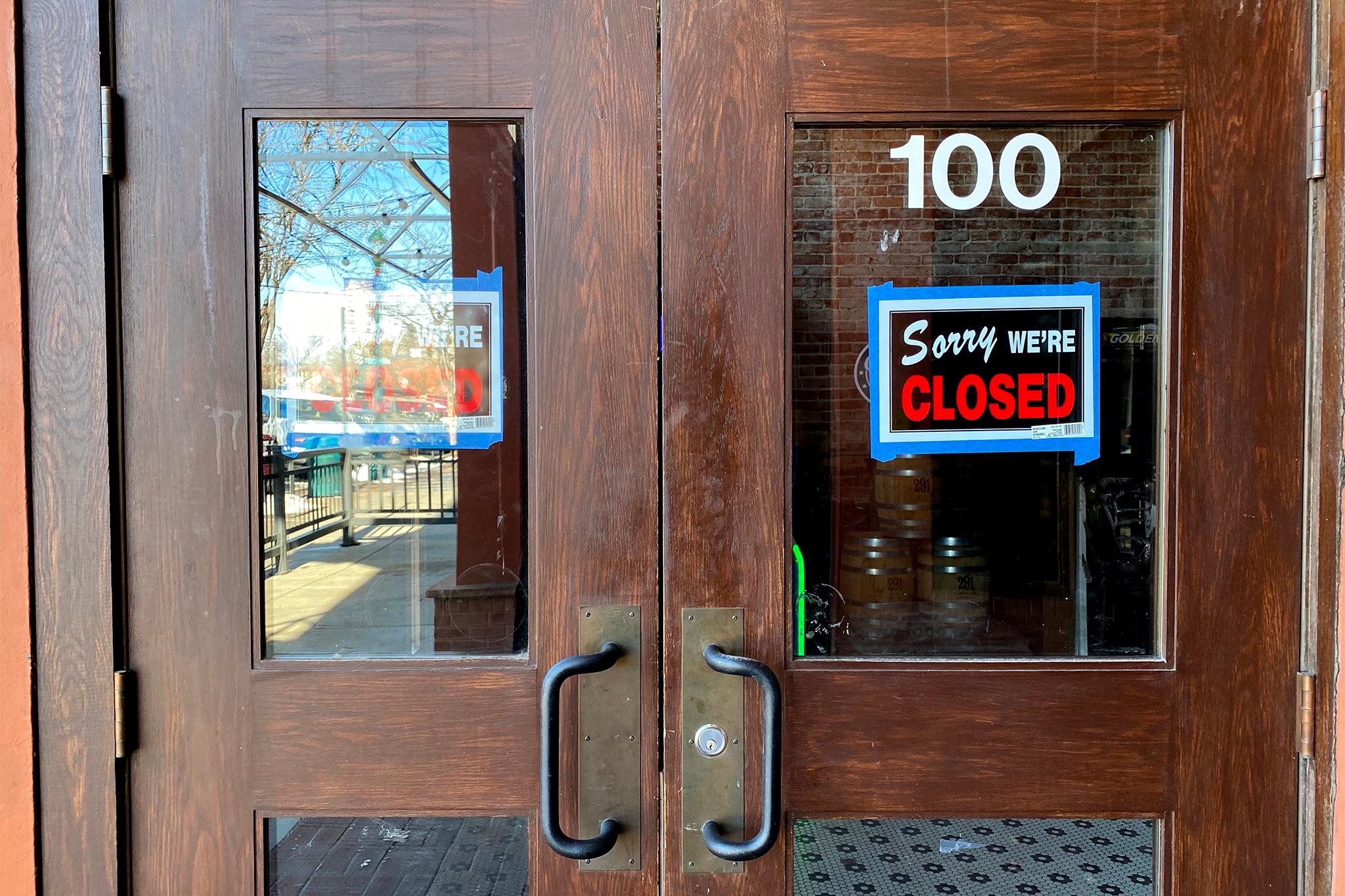 A set of wooden double doors have, in its two windows, "sorry we're CLOSED" signs taped to the glass.