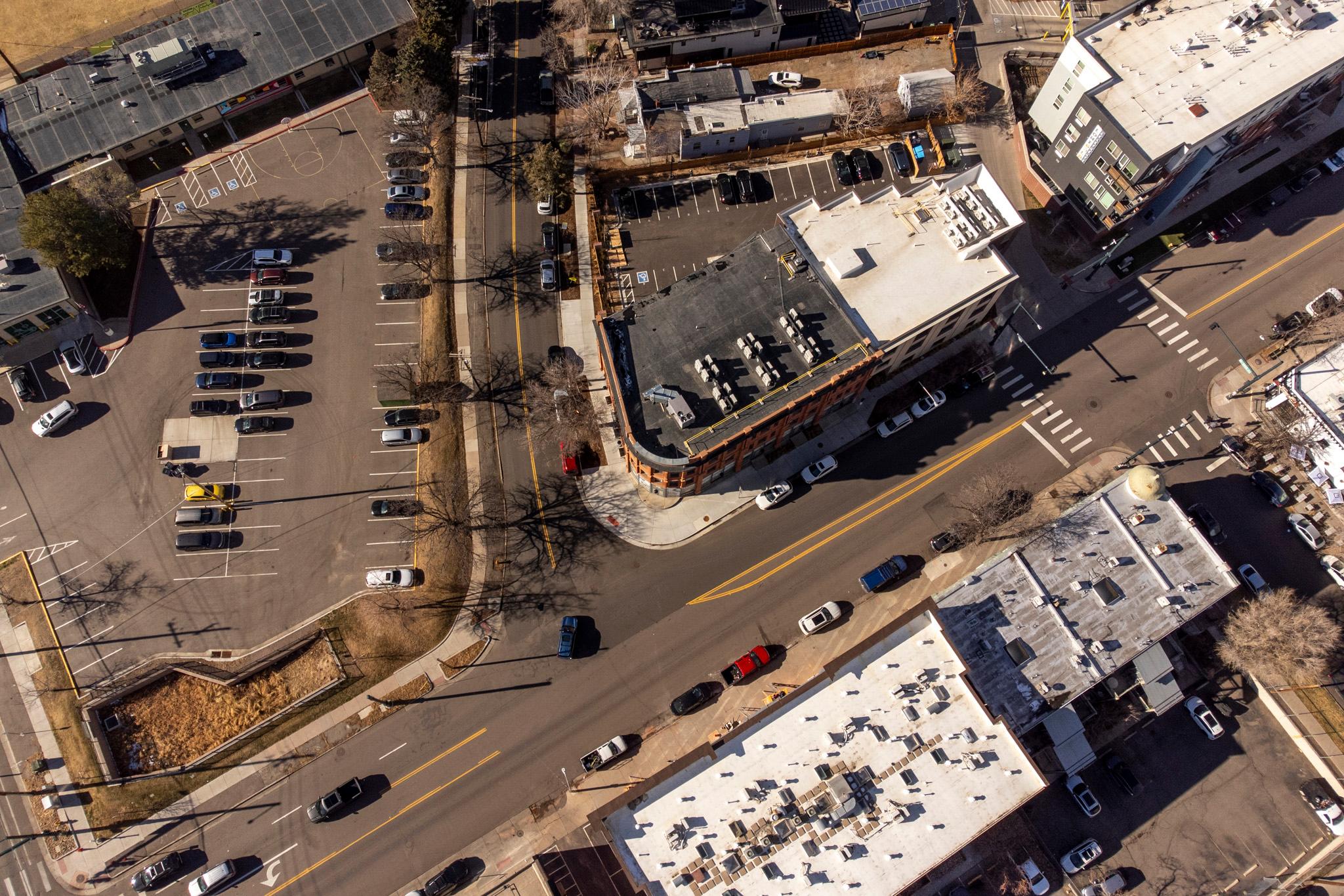 An aerial view of an intersection that's more of a 45 degree angle than the standard 90 degrees. Cars are parked all over the frame.