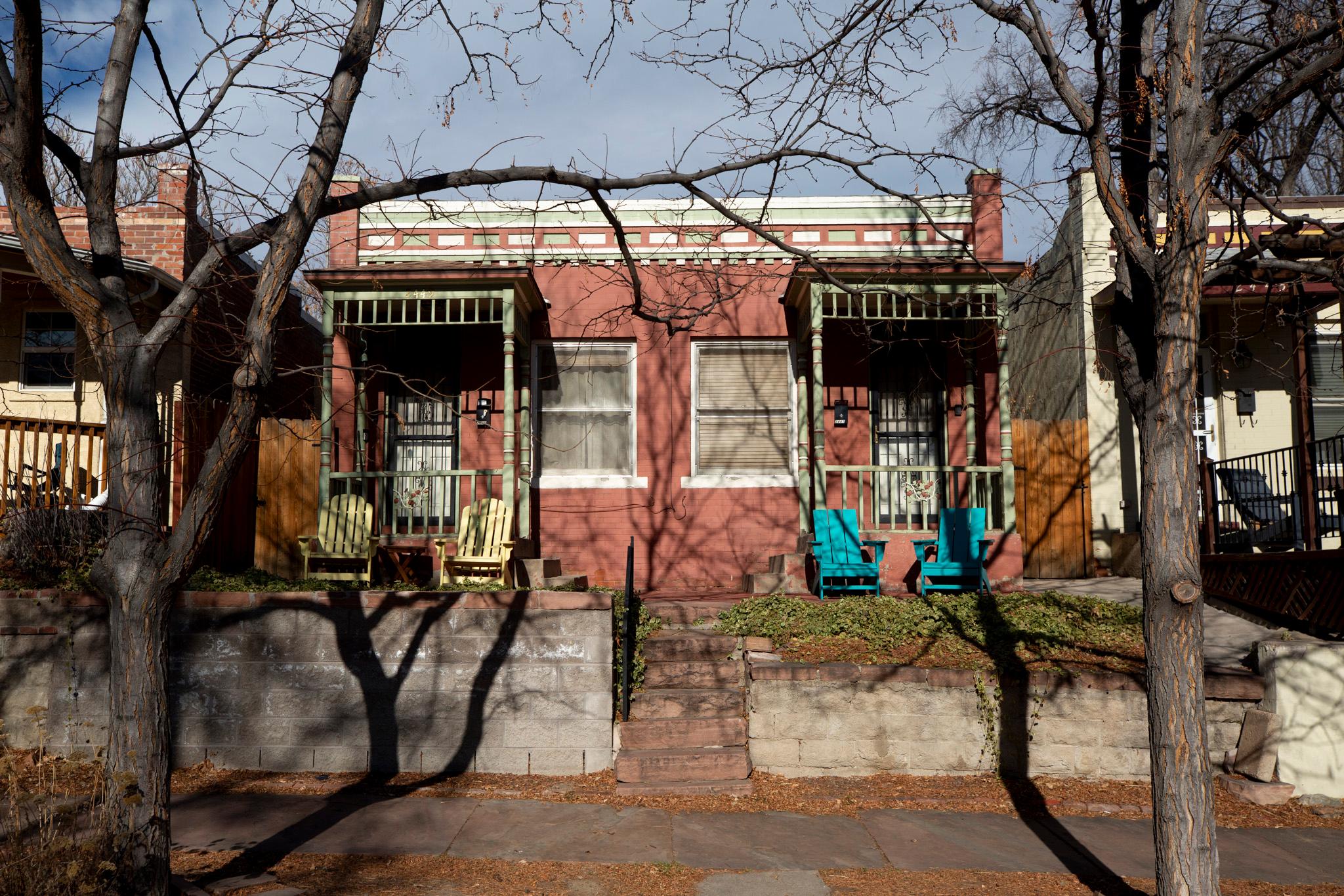 A squat red brick duplex sits above a tree-lined sidewalk.