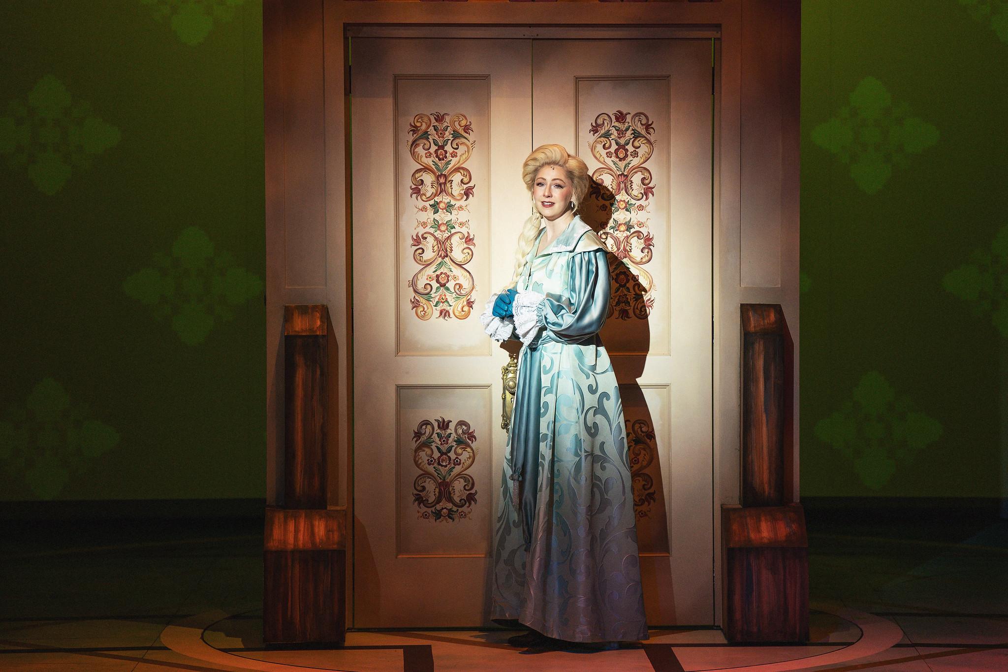 Women in light blue Elsa dress stands in front of ornate door.