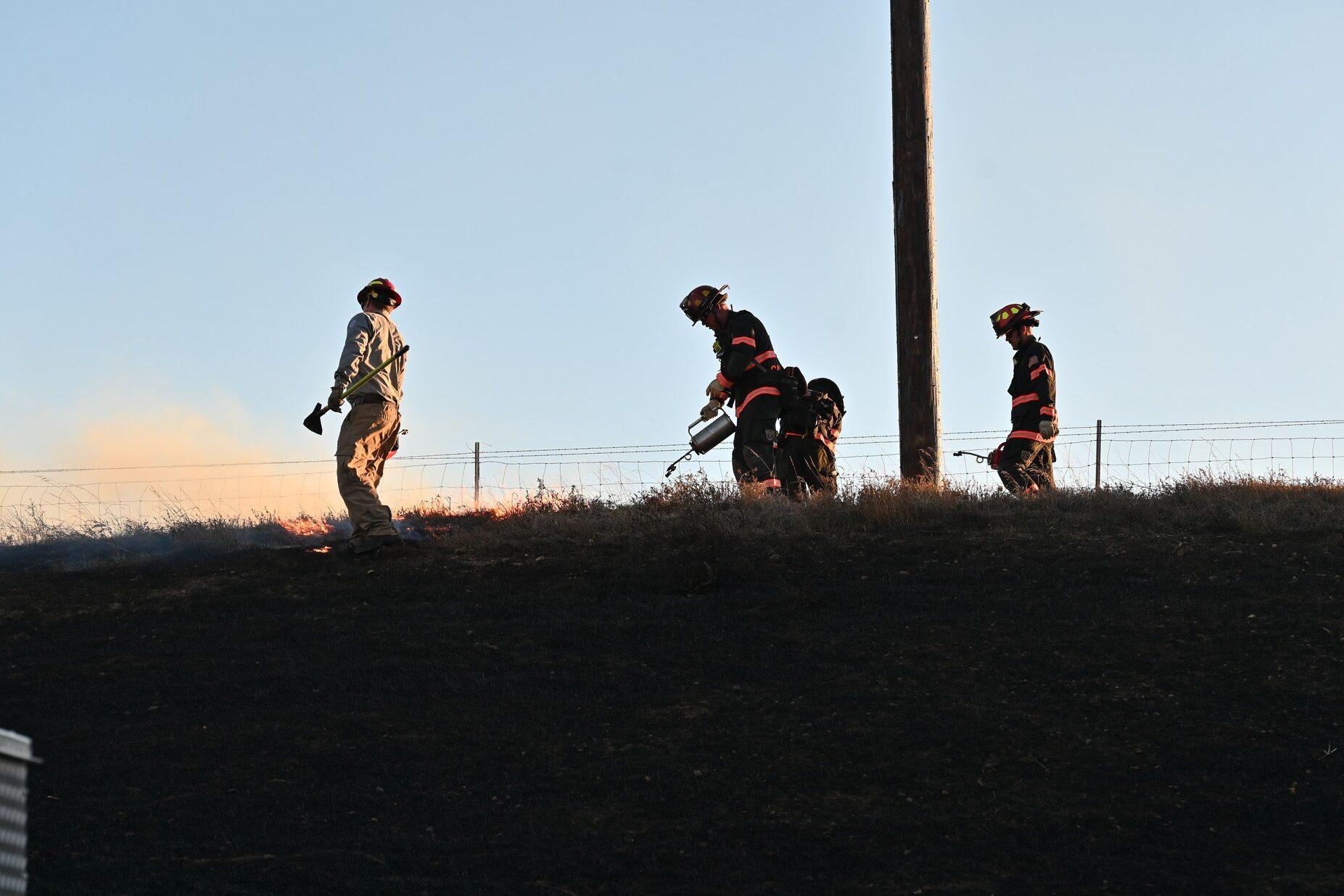 A group of firefighters is working together to put out a fire. They are standing on a hill, with one of them holding a fire extinguisher.