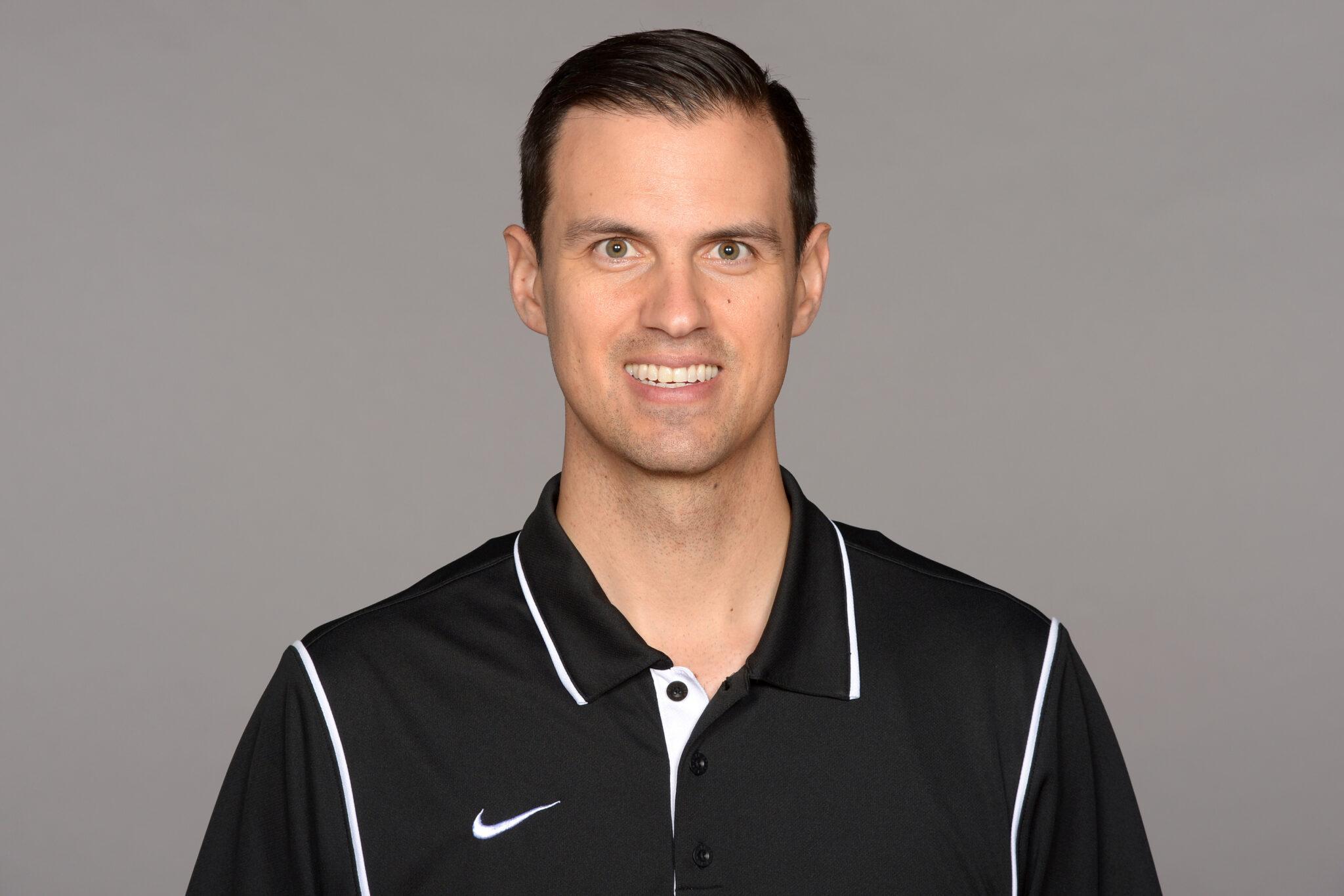 Fernando Lovo, waring a black Nike shirt, smiles and poses in front of a backdrop for a portrait.
