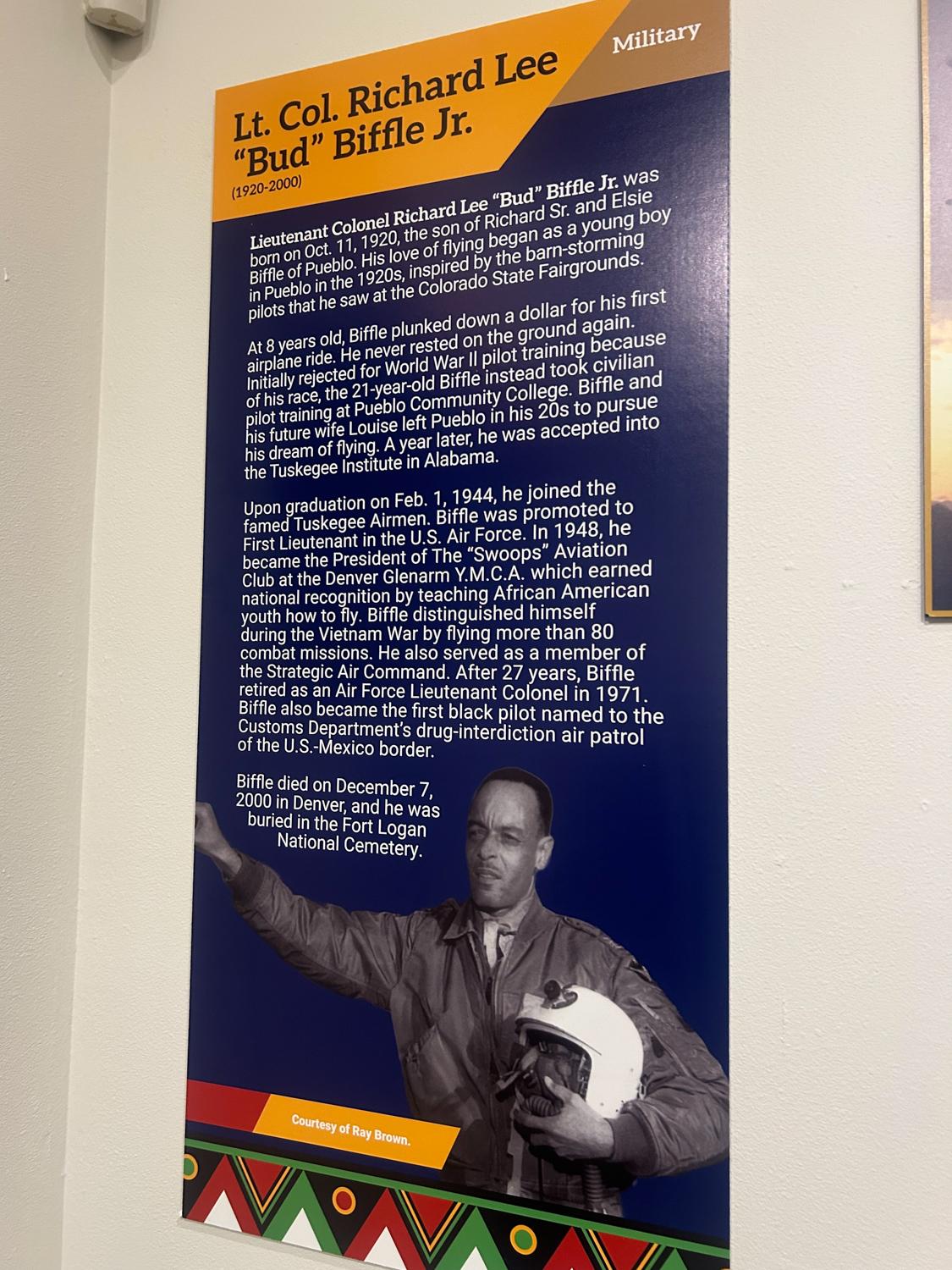 An exhibit featuring a man in a military uniform, holding a helmet and pointing upwards.