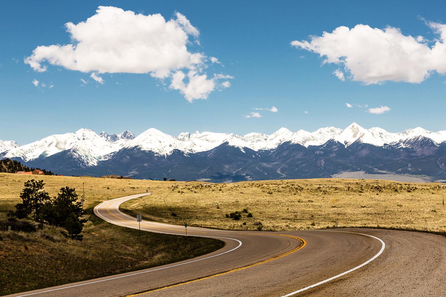 Curving paved roadway in an open area with snowcapped mountains in the distance.
