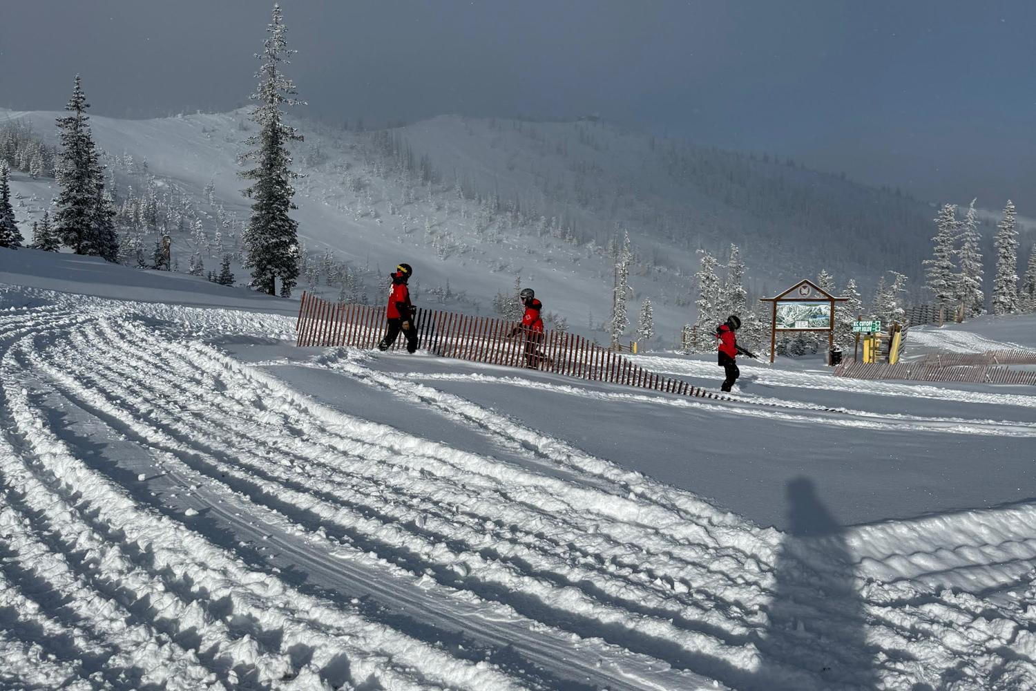 Three people in red ski jackets alongside a fence on a snow-covered slope.