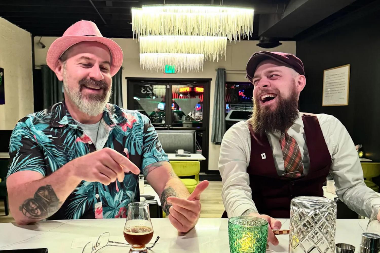 Two men sit at a table in a restaurant. They are laughing.