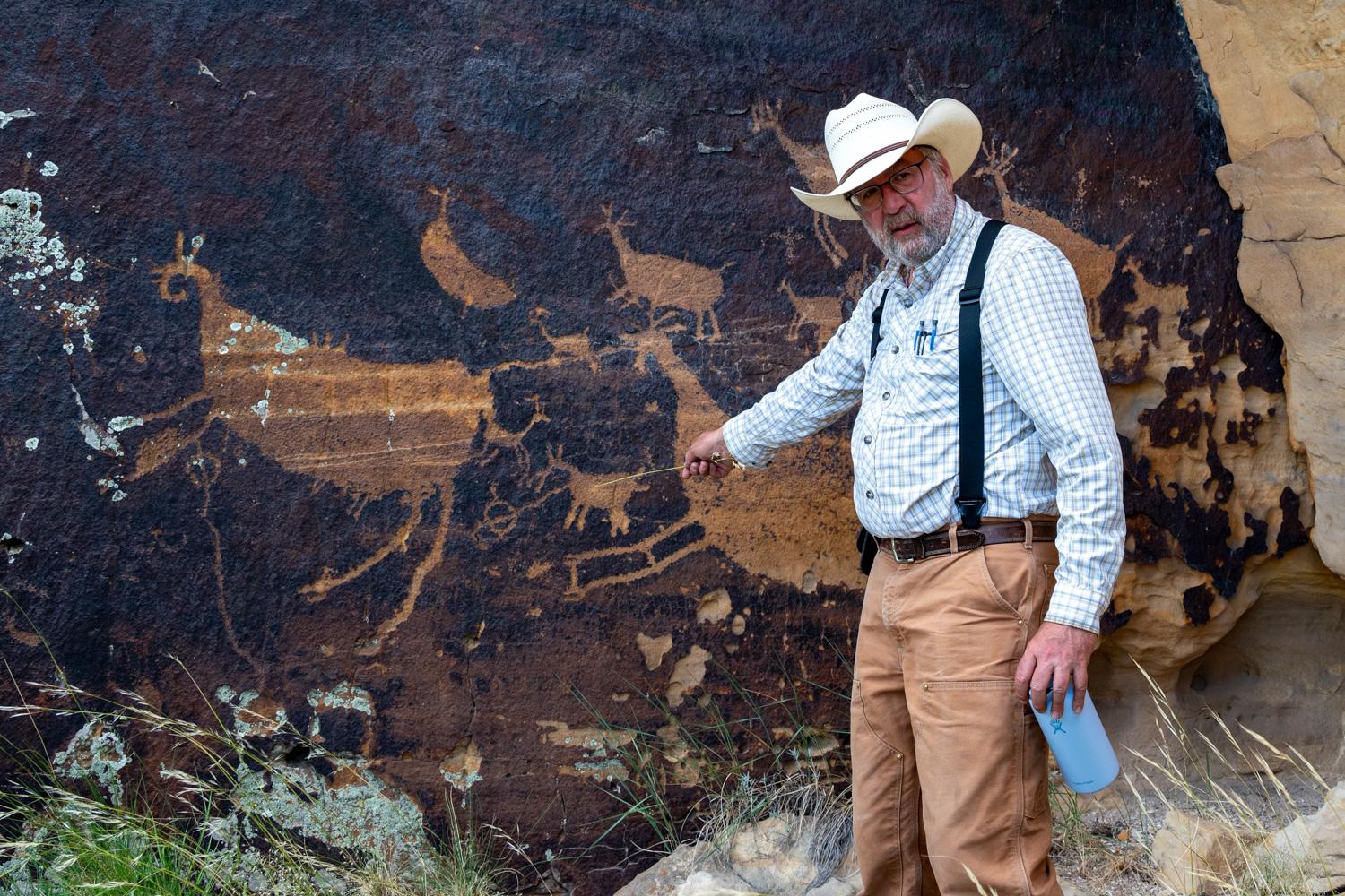 man with cowboy hat and beard in front of large images on a rock wall