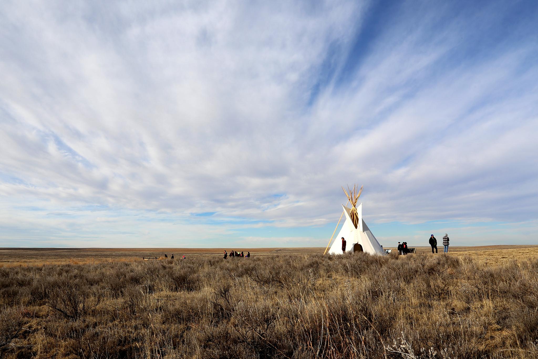 A tipi sits in a plan with a cloudy blue sky stretching along the top.