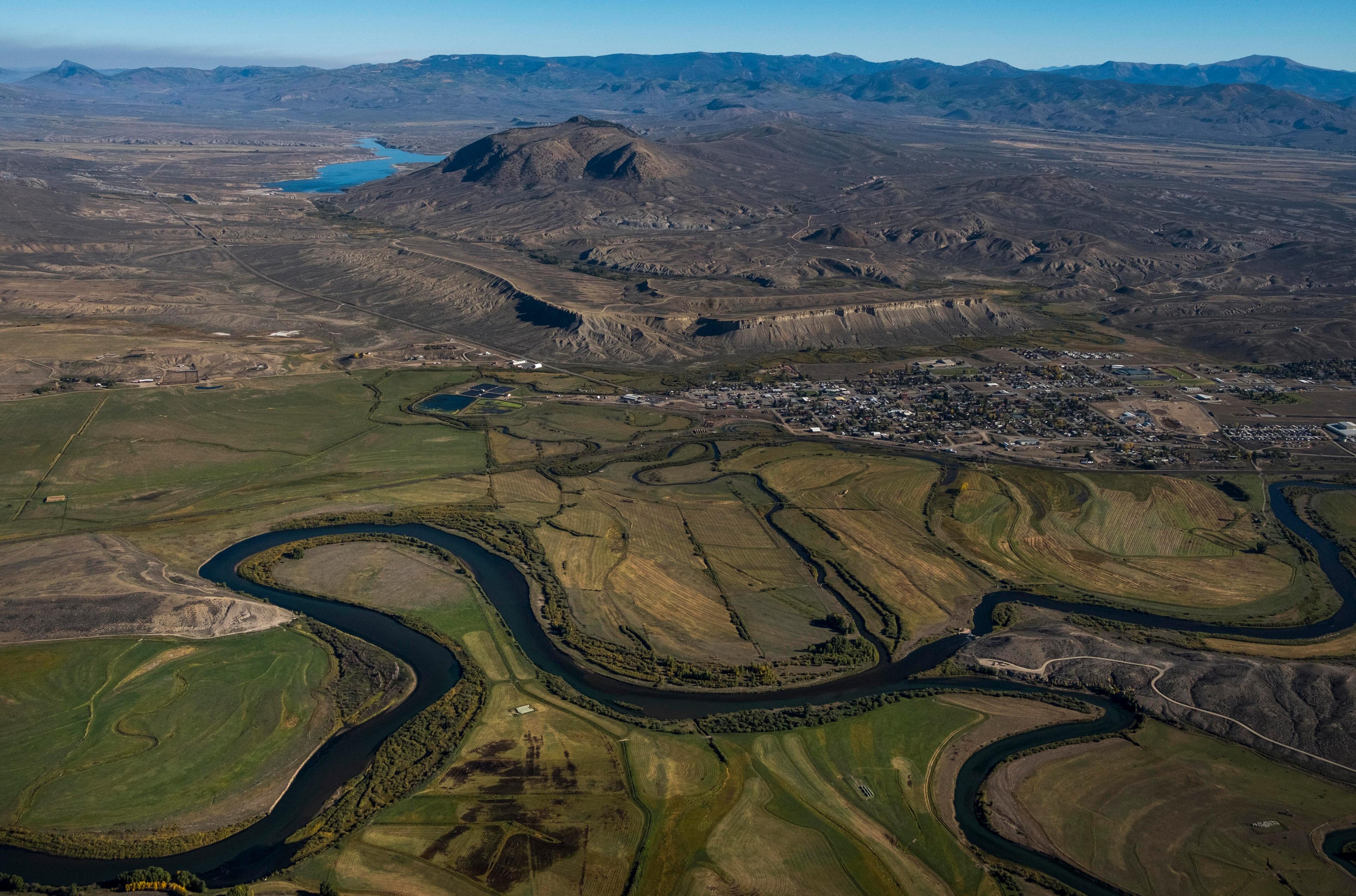 An photo taken from an airplane shows a river winding through a green valley with mountains behind it.