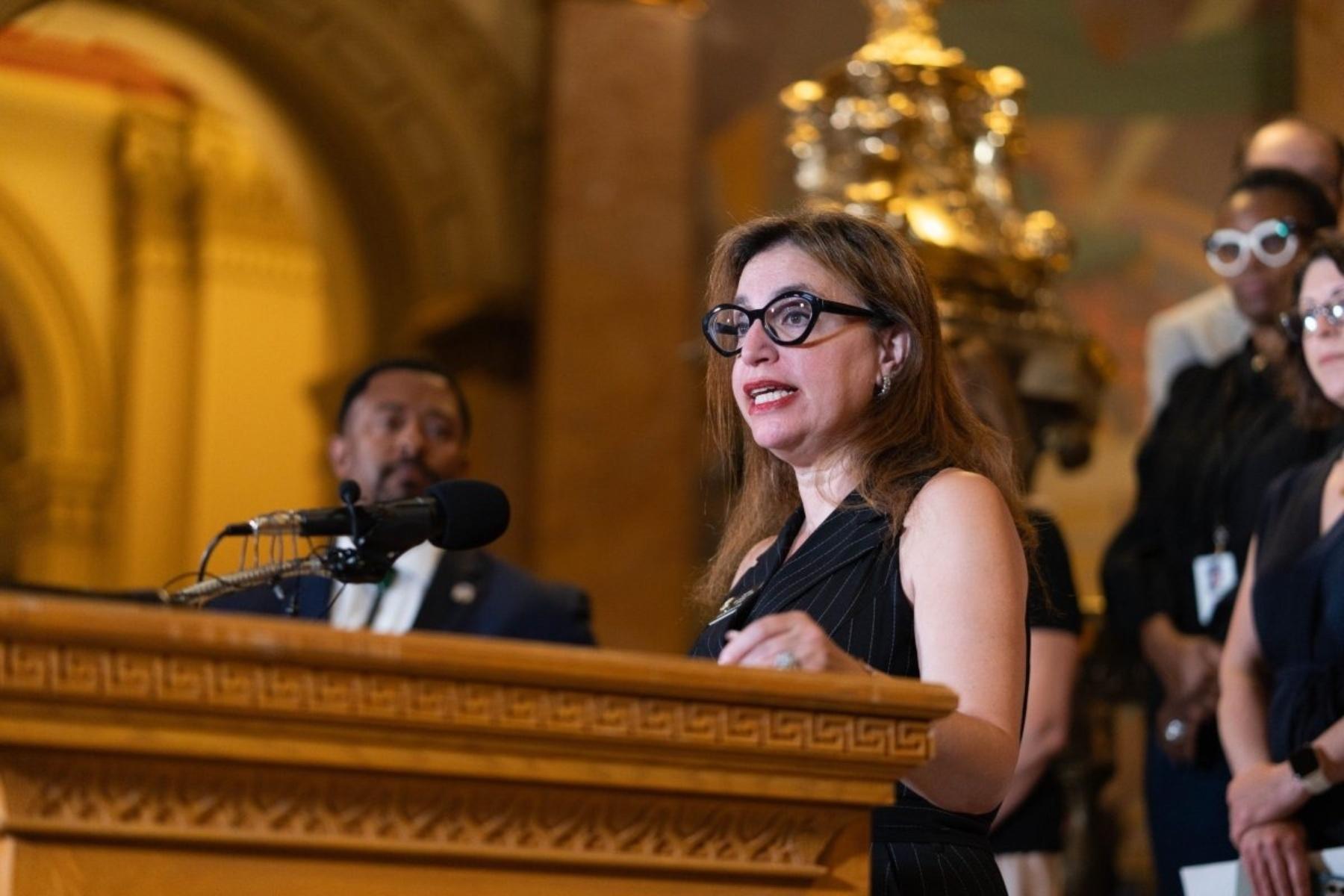 person in glasses at a podium looking off camera