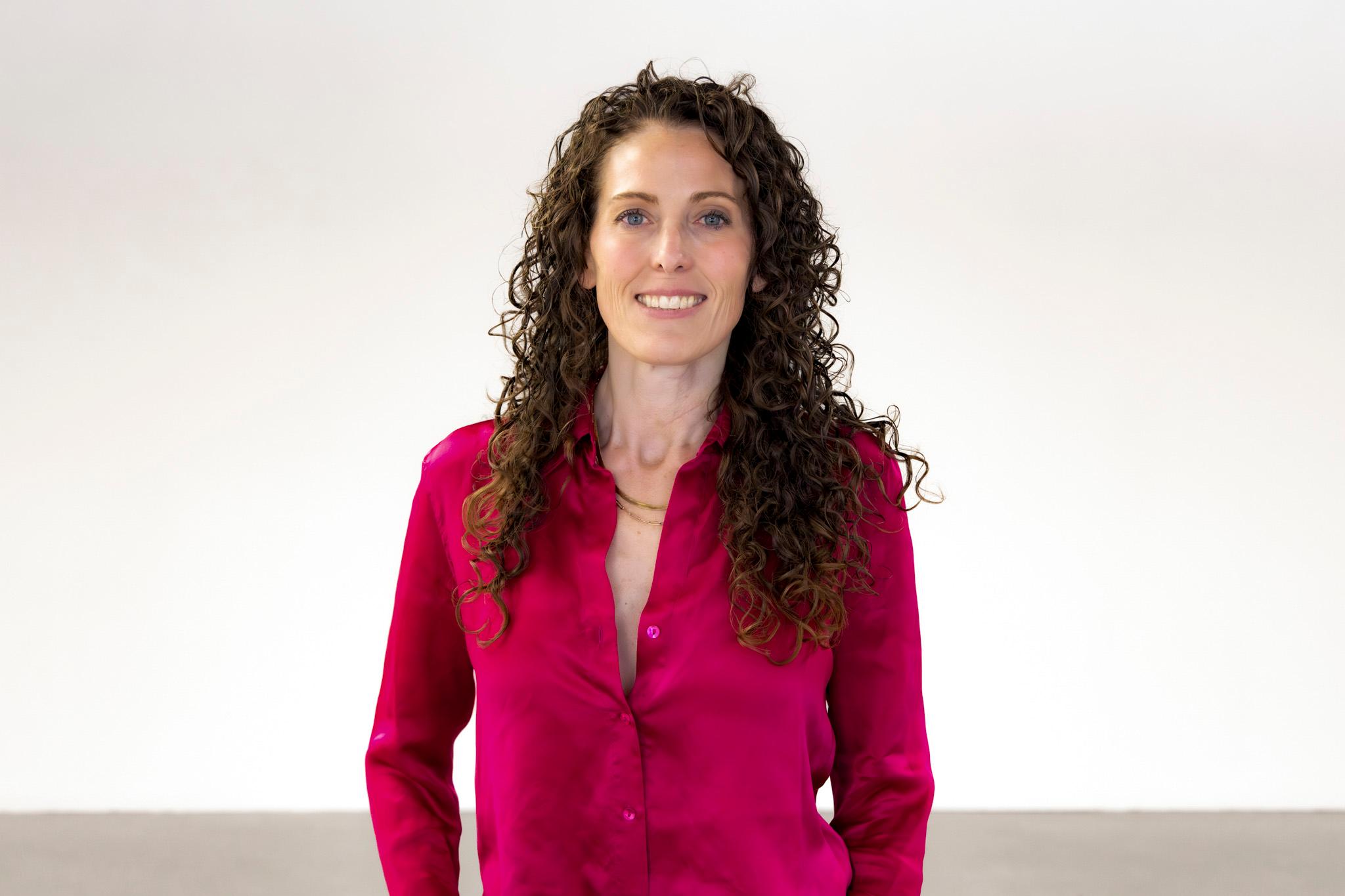 A woman in a red blouse stands in a white room.