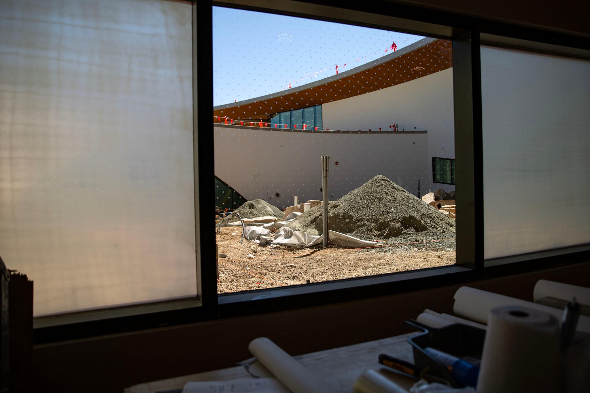 A pile of gravel can be seen through a glass window. Construction materials fill the foreground.
