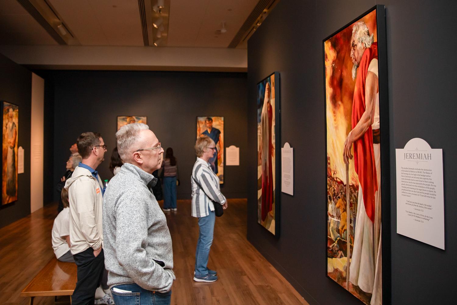 people look at colorful paintings in a room with dark walls and signs next to each painting