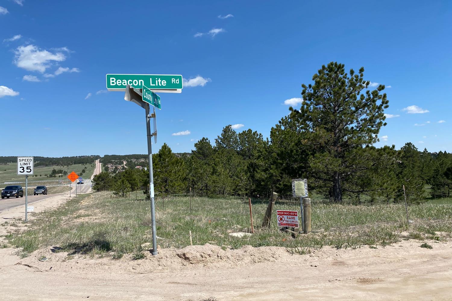 road signs at intersection of dirt and paved roads with pine trees in background