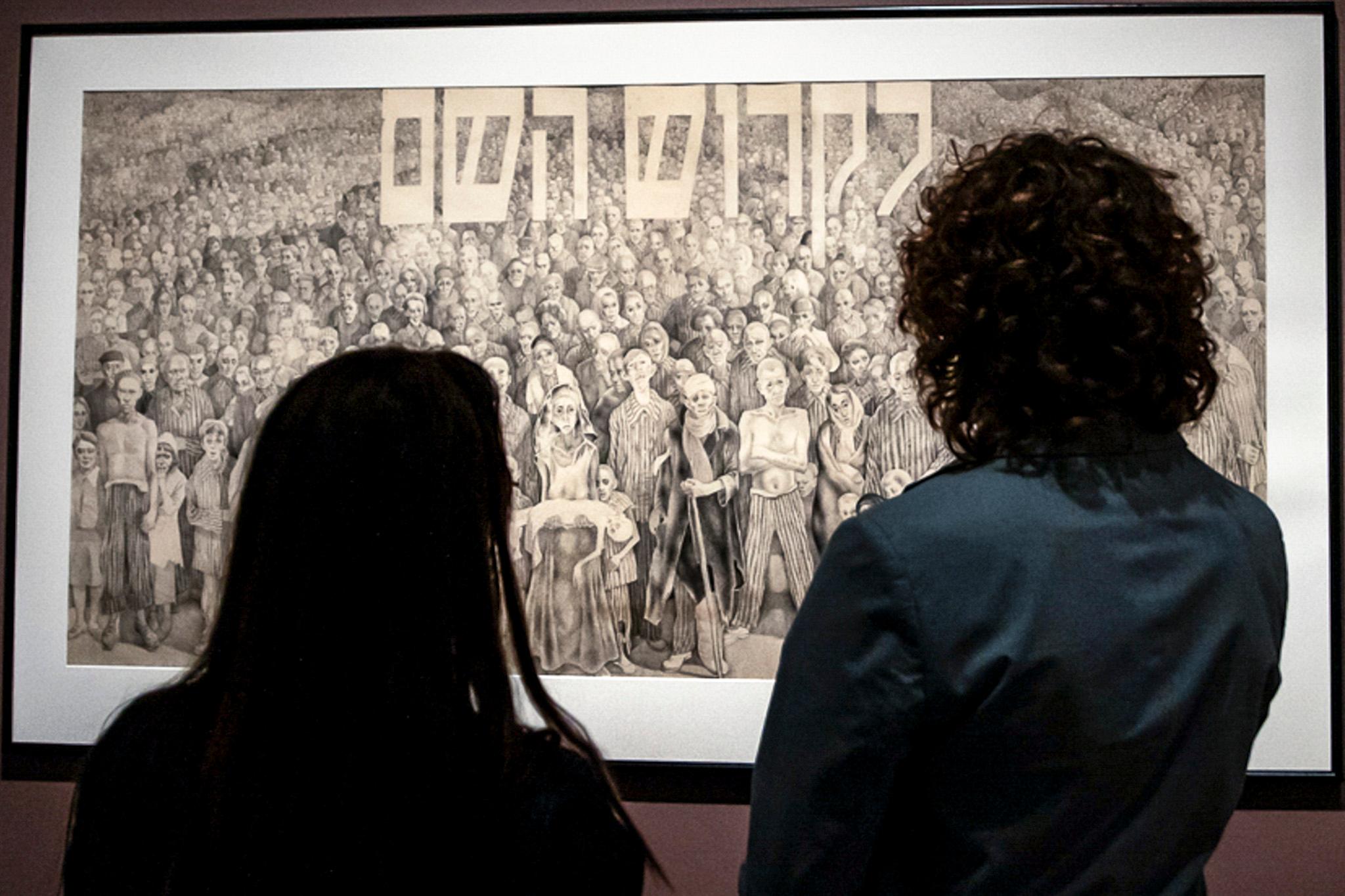 two people stand in front of a black and white sketch with hebrew lettering